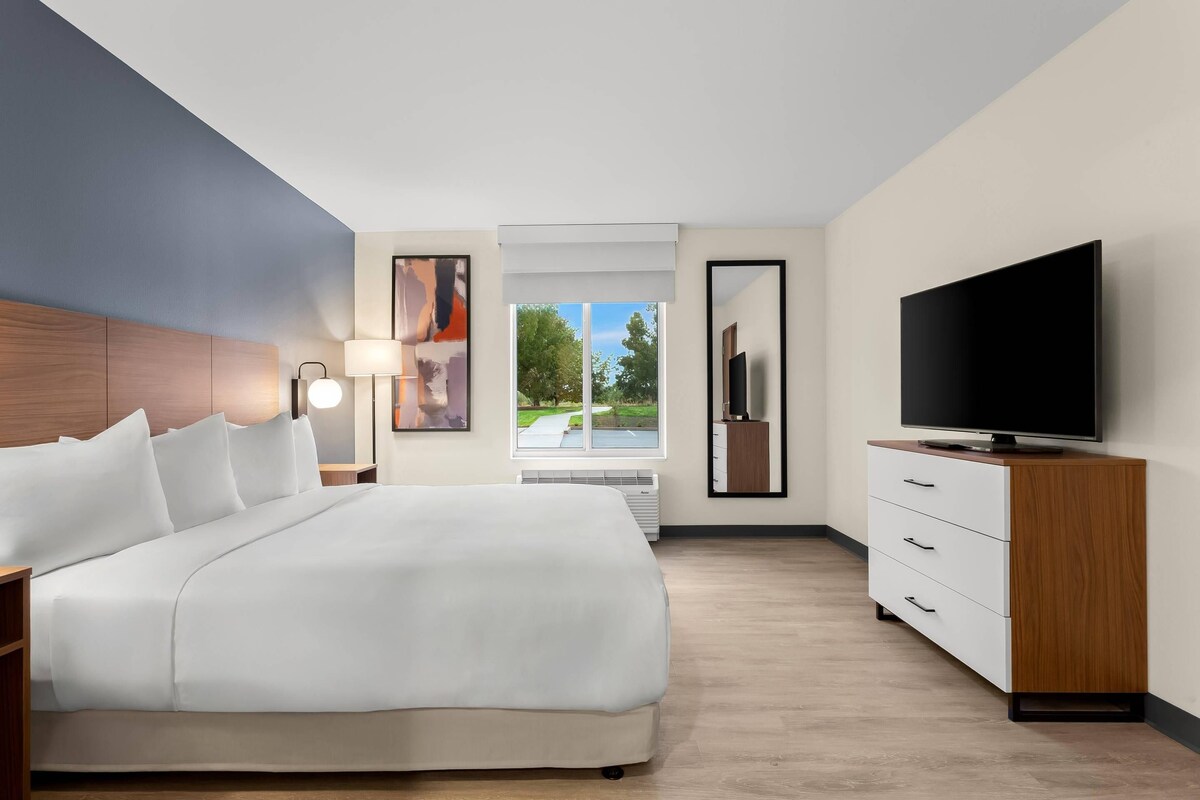 Una habitación de hotel con cama, televisión, lámpara y ventana con vistas al exterior.