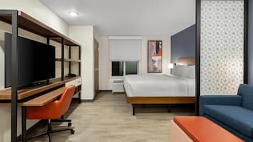 Une chambre d’hôtel comprenant un lit, un bureau avec une télévision, une chaise, un canapé et une cloison décorative ornée d’un motif géométrique.