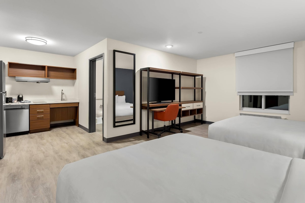Habitación de hotel con kitchenette, un escritorio con silla, dos camas y un ventanal grande.