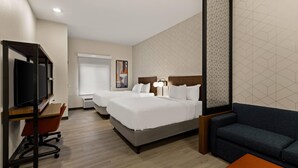 A hotel room with two beds, a desk with a chair, a sofa, and a TV.