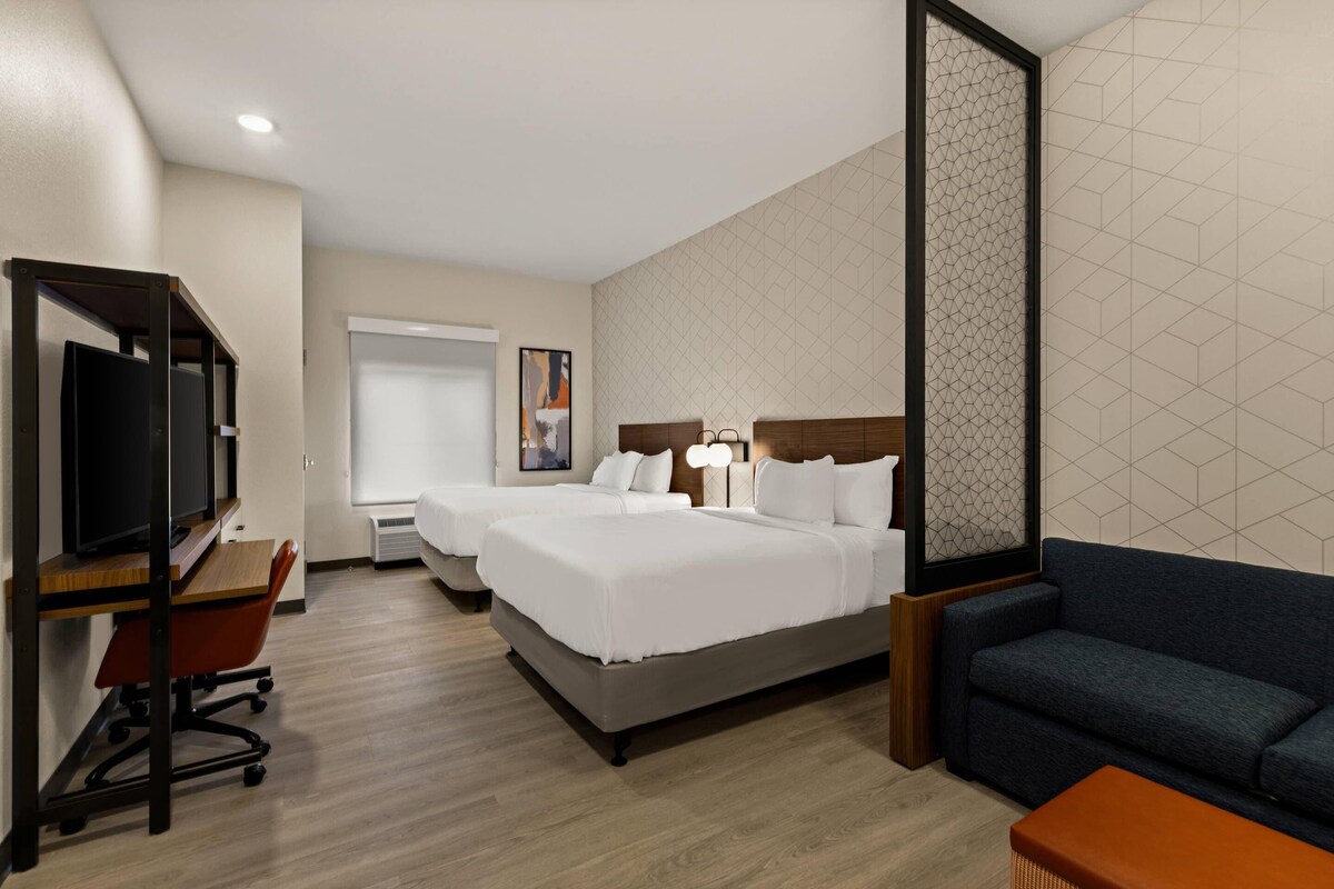 A hotel room with two beds, a desk with a chair, a sofa, and a TV.