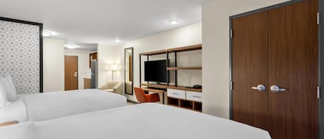 Ein Hotelzimmer mit zwei Betten, einem Schreibtisch, einem Stuhl, einem Fernseher und einem Kleiderschrank.
