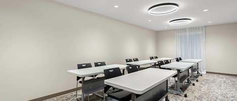 Une salle de conférence avec des tables et des chaises blanches, un sol recouvert de moquette et des spots encastrés au plafond.