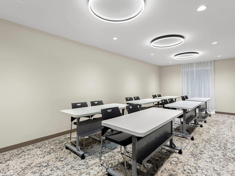 A conference room with white tables and chairs, a carpeted floor, and recessed ceiling lights.