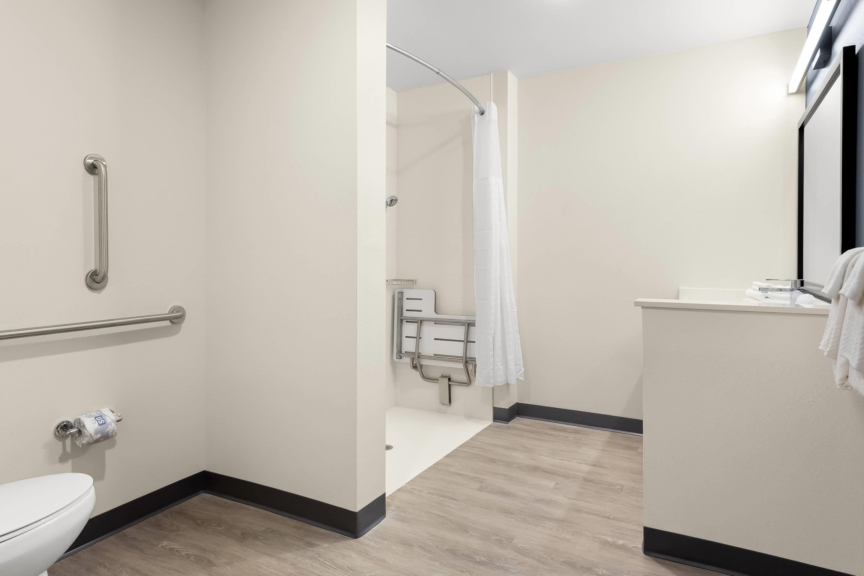 A modern bathroom with a toilet, grab bars, a shower with a curtain, and a sink with a towel.