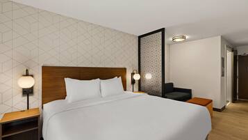 Ett modernt hotellrum med en stor säng, två sängbord, ett litet bord, en vägglampa och en avskärmning med ett geometriskt mönster.