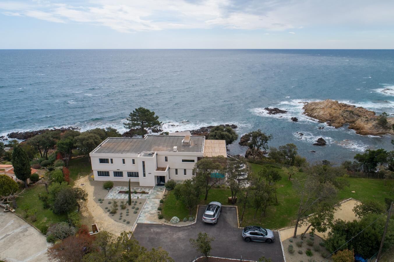 Una casa moderna de dos plantas con techo plano, rodeada de un jardín ajardinado y vista al océano.