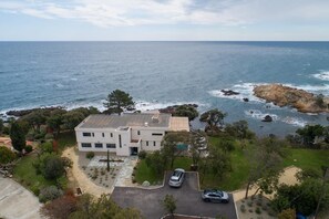 A modern two-story house with a flat roof, surrounded by a landscaped garden and a view of the ocean. - Stunning waterfront villa with a private beach in CANELLA (Sari-Solenzara)