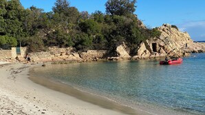 A beach with clear water, a rocky outcrop, and a red boat. - Stunning waterfront villa with a private beach in CANELLA (Sari-Solenzara)