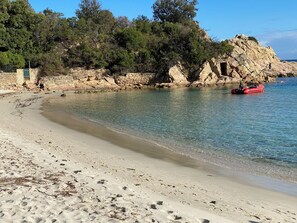 A beach with clear water, a rocky outcrop, and a red boat. - Stunning waterfront villa with a private beach in CANELLA (Sari-Solenzara)