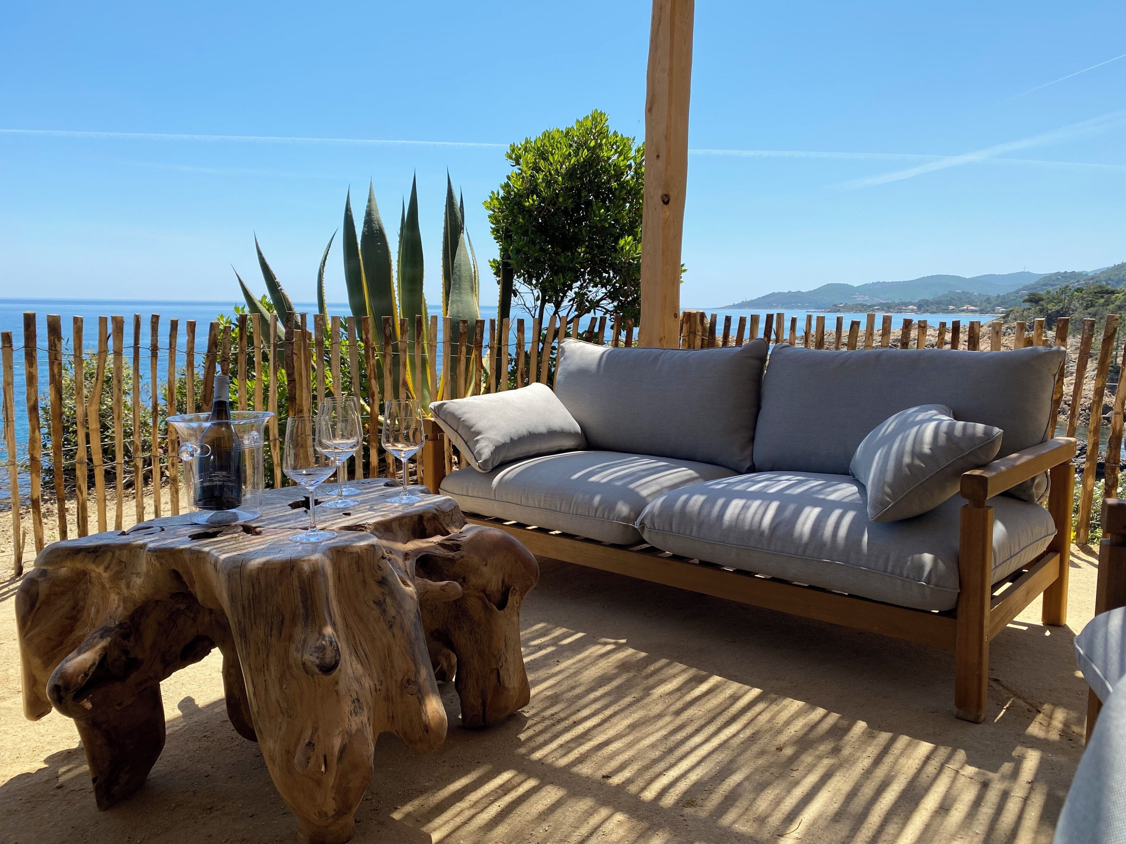 A wooden deck with a sofa and table, overlooking a coastal landscape.