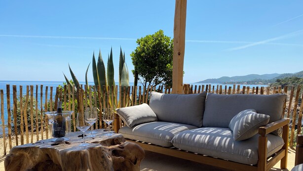 A wooden deck with a sofa and table, overlooking a coastal landscape. - Stunning waterfront villa with a private beach in CANELLA (Sari-Solenzara)