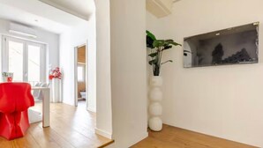 A hallway with a wooden floor, a red chair, a white vase with plants, and a framed picture on the wall. - Apartment in Central Florence Near the Duomo (Florence)