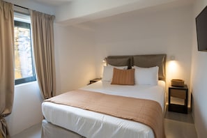 Ein Schlafzimmer mit Bett, Vorhängen, einem Nachttisch, einer Lampe und einer Steinwand.