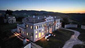 A large, multi-story building with a symmetrical facade, a central courtyard with seating, and a surrounding landscape.