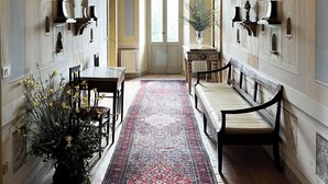 A hallway with a patterned rug, benches, a table, and a potted plant.