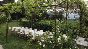 A garden setting with a long table and chairs, surrounded by lush greenery and flowering plants.