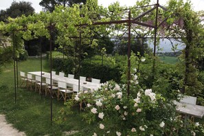 Un jardin aménagé avec une longue table et des chaises, entouré d’une végétation luxuriante et de plantes en fleurs.
