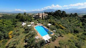 An aerial view of a property with a swimming pool, surrounded by lush greenery and a mountainous backdrop.