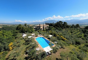 Une vue aérienne d’une propriété dotée d’une piscine, entourée d’une végétation luxuriante et ayant une chaîne de montagnes en arrière-plan.