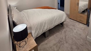 Een slaapkamer met een bed, nachtkastje, lamp, kledingkast en een spiegel.