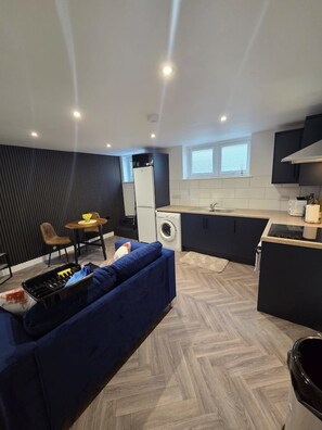 A compact kitchen with a dining area, a washing machine, and a sofa.