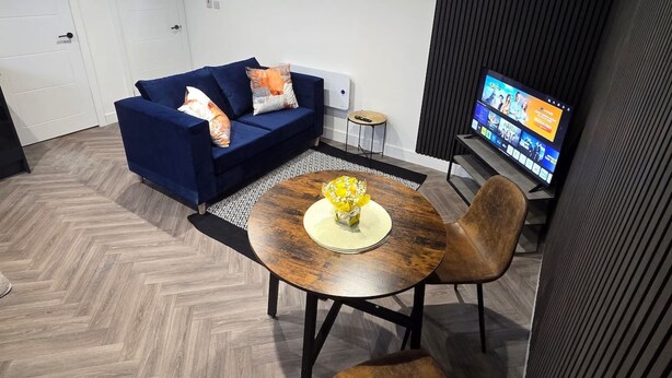 Een moderne woonkamer met een blauwe bank, een houten salontafel met een gele decoratie, en een televisie op een meubel.