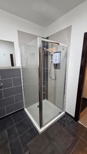 A modern bathroom with a glass-enclosed shower, dark tiled flooring, and a white wall with a power outlet. - The Family Flat by JS Apartments (Blackburn)