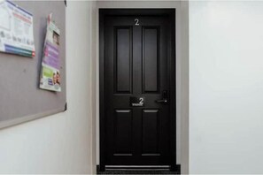 Eine schwarze Tür mit der Nummer 2, ein Bulletin Board mit Unterlagen und eine helle Wand.