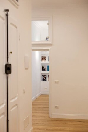 Un passadís amb parets blanques, un sòl de fusta i una porta a l'esquerra.