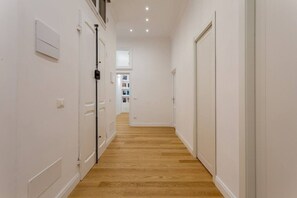 A narrow hallway with wooden flooring, white walls, and closed doors.