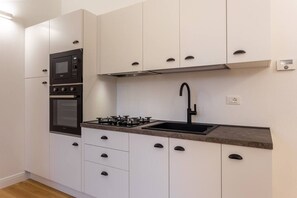 Eine moderne Küche mit weißen Schränken, einem eingebauten Ofen, einem Gasherd und einem schwarzen Spülbecken.