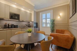 Eine moderne Küche mit Einbauofen, eine Essecke mit rundem Tisch und Stühlen sowie eine Sitzecke mit einer Couch.