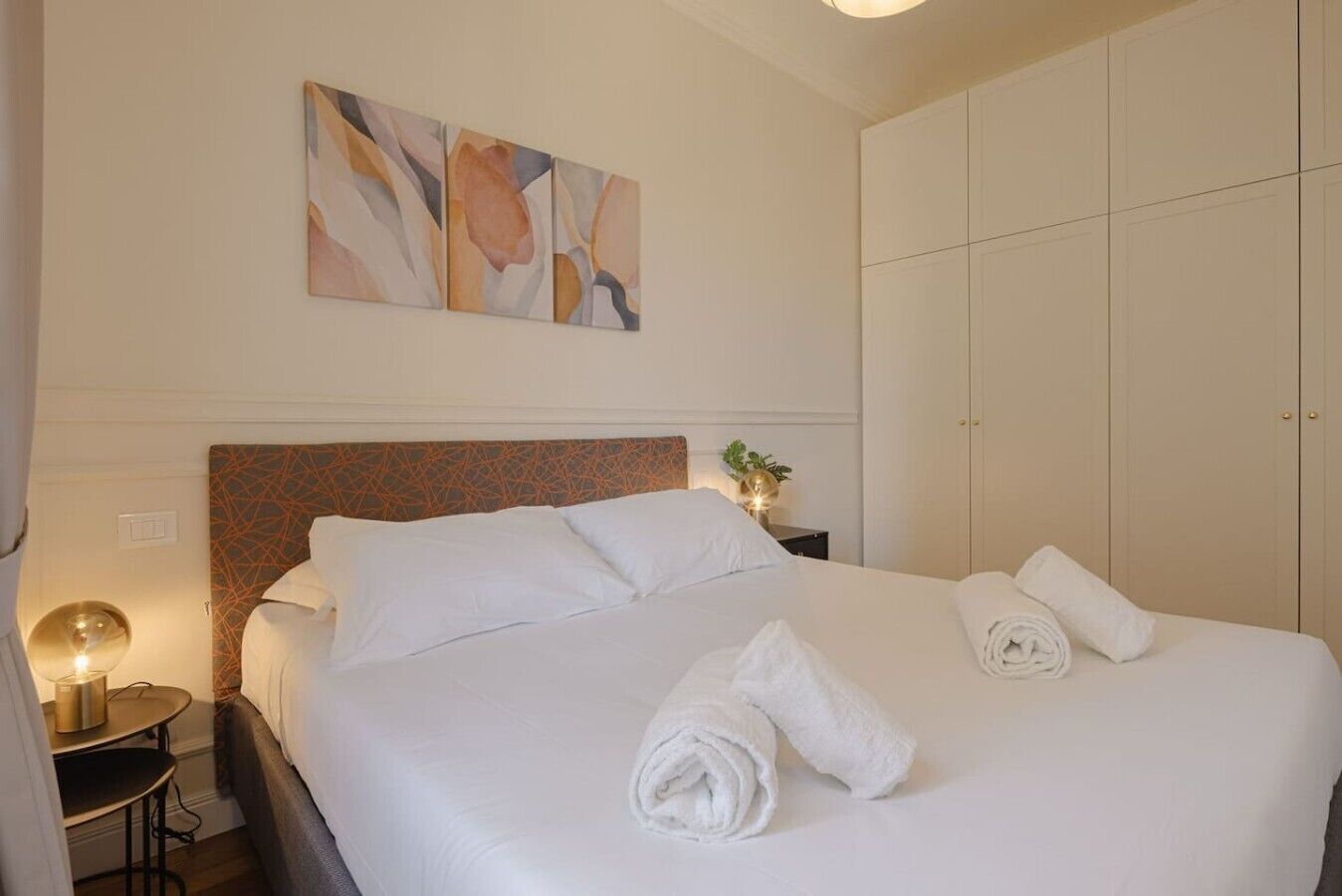 A hotel room with a bed, a nightstand, a lamp, and a wardrobe.