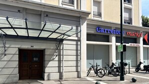 Rakennuksessa on lasinen sisäänkäynti, ovi, jonka yläpuolella on numero 2, ja pysäköintikyltti, joka osoittaa pyöräpysäköintialueen.