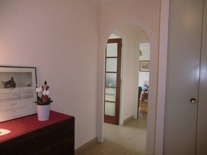 Ein Flur mit einer zur Zimmer führenden Tür, einem gerahmten Bild auf einer Kommode und einem Blumentopf.