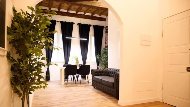 Una habitación con suelo de madera, un sofá, una mesa de comedor con sillas y una planta en maceta.