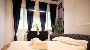 Habitación de hotel con cama, dos sillas, escritorio, planta en maceta y ventana con cortinas.