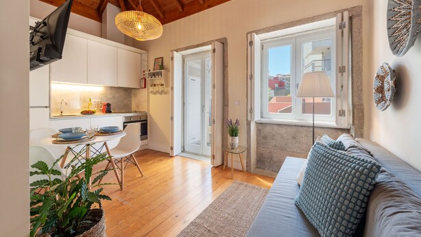 Un interno moderno con soffitto in legno, un'area pranzo con tavolo e sedie, un divano con cuscini decorati e una vista attraverso una porta aperta.