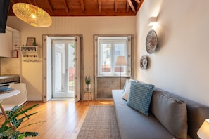 Ein modernes Wohnzimmer mit einer Couch, einem Esstisch und einer durchgehenden Tür erkennbaren Küchenzeile.