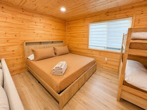 Une chambre dans un chalet en bois, avec un lit superposé, un lit simple et une fenêtre.