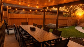 An outdoor patio with a wooden table and chairs, string lights, and a wooden fence. - Rock House/Riverfront/EV Charging/Large Groups (Kernville)