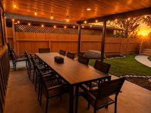 Eine Terrasse im Freien mit Holztisch und -stühlen, Lichterketten und einem Holzzaun.