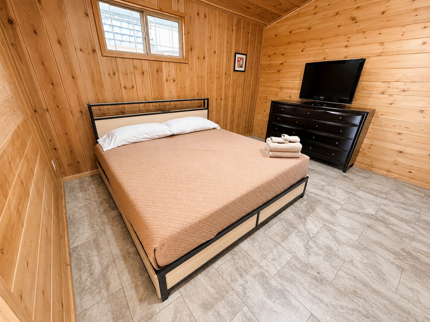 A wooden-paneled room with a bed, a dresser, and a television.
