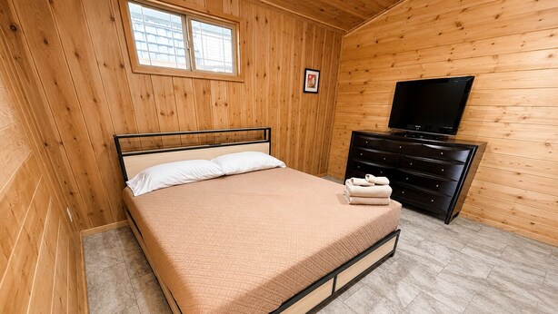 A wooden-paneled room with a bed, a dresser, and a television. - Rock House/Riverfront/EV Charging/Large Groups (Kernville)