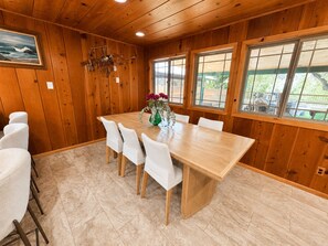 A dining area with a wooden table and chairs, a vase with flowers, and large windows.