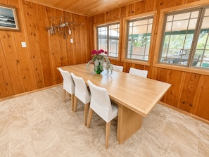 A wooden-paneled room with a large dining table, white chairs, and a vase with flowers.