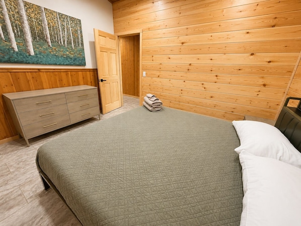 A room with a bed, a dresser, a painting, and a wooden wall.
