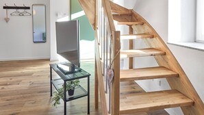 Escada espiral de madeira em um interior moderno, com uma televisão de tela plana e uma pequena mesa com uma planta.