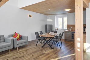 Een moderne woonkamer met een eettafel, grijze banken en een keukenhoek.